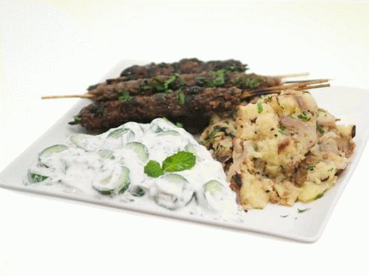 Fotografija jagnjetine Kufte na nabodalih z granatno glazuro, krompirjem z bengalskimi začimbami in omako raita.